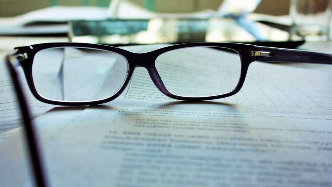 Glasses sitting on an employee contract with a mandatory arbitration agreement, employee researching how to report sexual harassment in the workplace